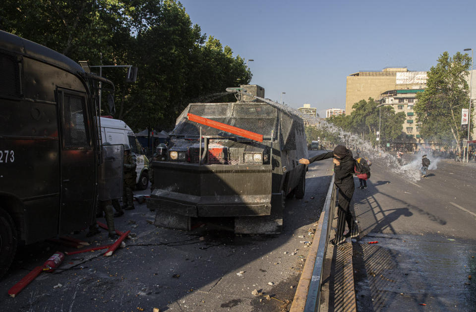 A protester throws a board at a water cannon during clashes with police in front of the Santa Lucia subway station during a protest against the rising cost of subway and bus fares, in Santiago, Friday, Oct. 18, 2019. (AP Photo/Esteban Felix)