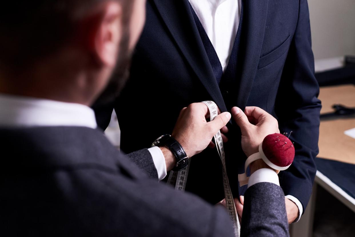 Over shoulder view of bearded fashion designer fitting bespoke suit to model, close-up shot