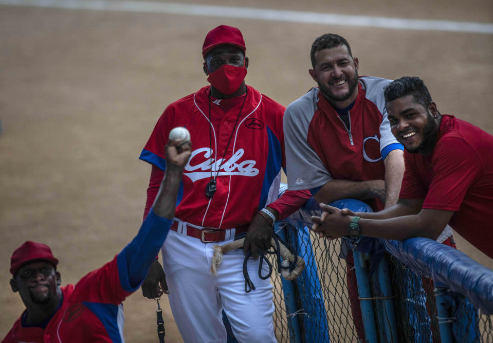 Cuba's pitcher Yoanni Yera Montalvo, left, throws the ball as his teammates smile watching him during a training session at the Estadio Latinoamericano in Havana, Cuba, Tuesday, May 18, 2021. A little over a week after the start of the Las Americas Baseball Pre-Olympic in Florida, the Cuban team does not have visas to travel to the United States. At second from right is Lazaro Blanco. (AP Photo/Ramon Espinosa)