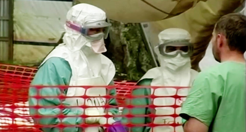 Doctors in protective clothing that protects them against the Marburg virus are seen speaking to a man.