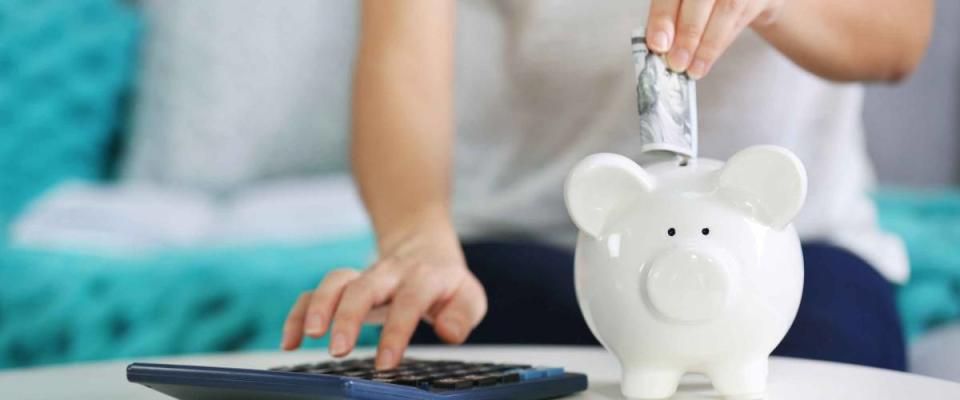 Female hand putting money into piggy bank and counting on calculator closeup