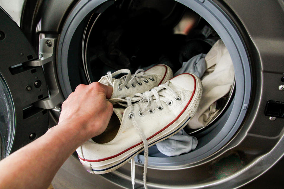 Männerhand legt Schuhe in die Waschmaschine. 