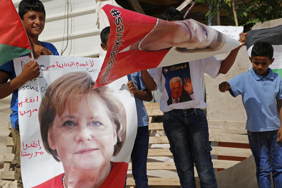 Bedouin children hold pictures of German Chancellor Angela Merkel ahead of her expected visit to Israel on Wednesday, in the West Bank Bedouin community of Khan al-Ahmar, Tuesday, Oct. 2, 2018. The children are pleading with Merkel to pressure Israel to halt demolition plans for the encampment of corrugated shacks outside an Israeli settlement east of Jerusalem. Arabic on the poster reads, "save Khan al-Ahmar" and "save our school." (AP Photo/Nasser Shiyoukhi)