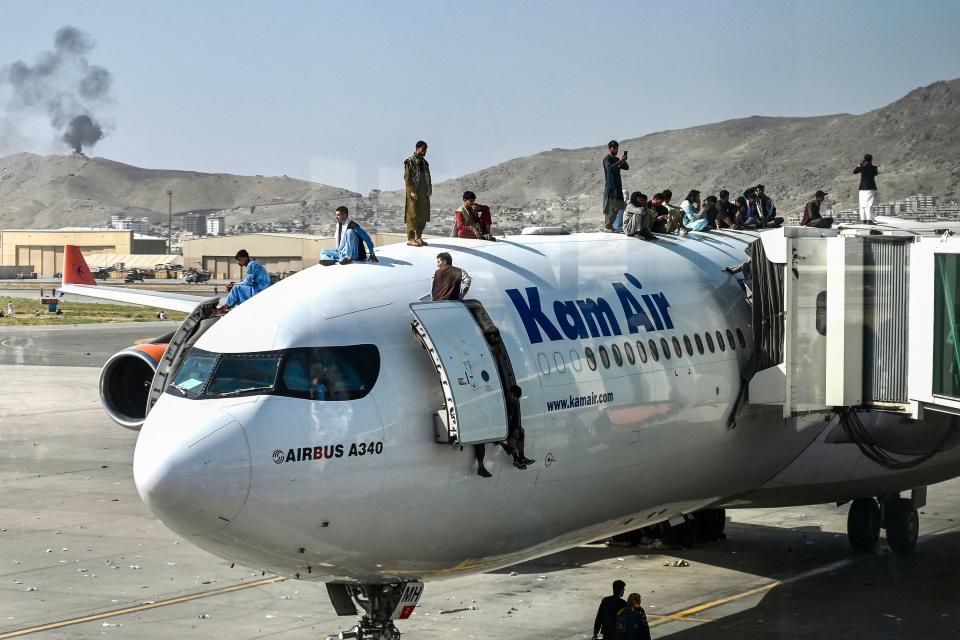 Afghan people climb atop a plane as they wait at the Kabul airport in an attempt to flee the Taliban's feared hardline brand of Islamist rule