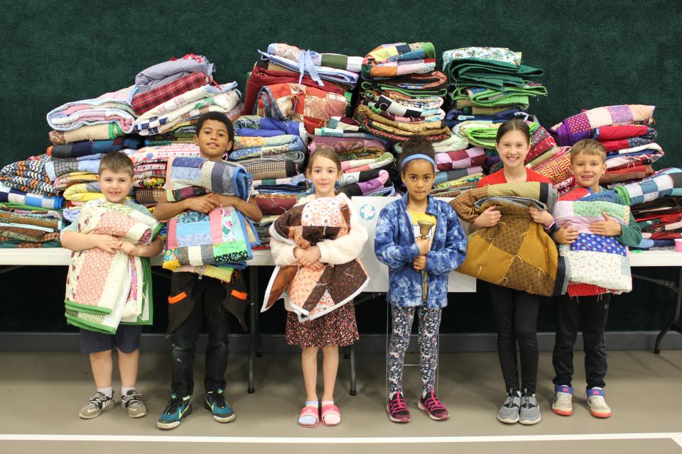 From left, Elijah King, Isaac Obri, Allison Hochstetler, Chloe Obri, Mara Steiner and Harris Steiner hold comforters and stand in front of stacks of completed comforters at the 2023 Ohio MCC Comforter Bash.