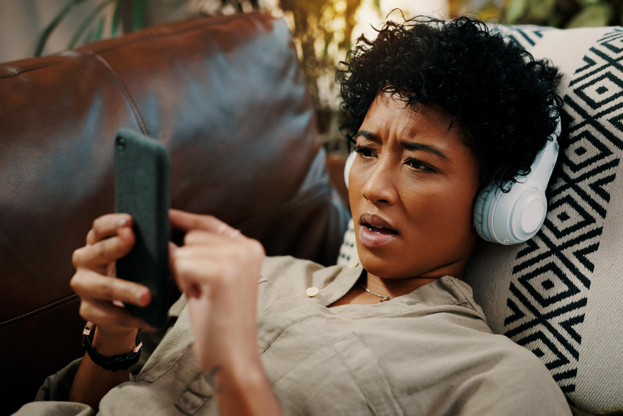 Shot of a young woman wearing headphones while using her cellphone at home