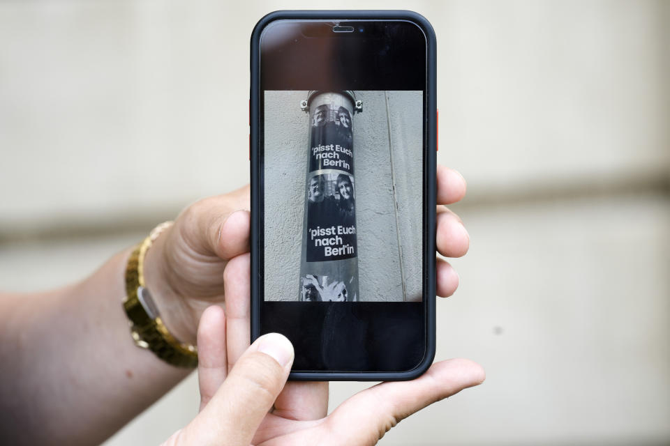 Teacher Laura Nickel shows her cell phone with pictures of stickers on a lamp pole showing images of her and colleague Max Teske with the caption "piss off to Berlin" during an interview with The Associated Press in Cottbus, Germany, Wednesday, July 19, 2023. Two teachers in eastern Germany tried to counter the far-right activities of students at their small town high school. Disheartened by what they say was a lack of support from fellow educators, Laura Nickel and Max Teske decided to leave Mina Witkojc School in Burg. (AP Photo/Markus Schreiber)