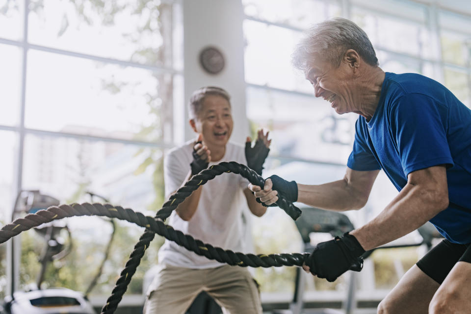 Asian Chinese Senior personal trainer encouraging senior man practicing battle rope in gym