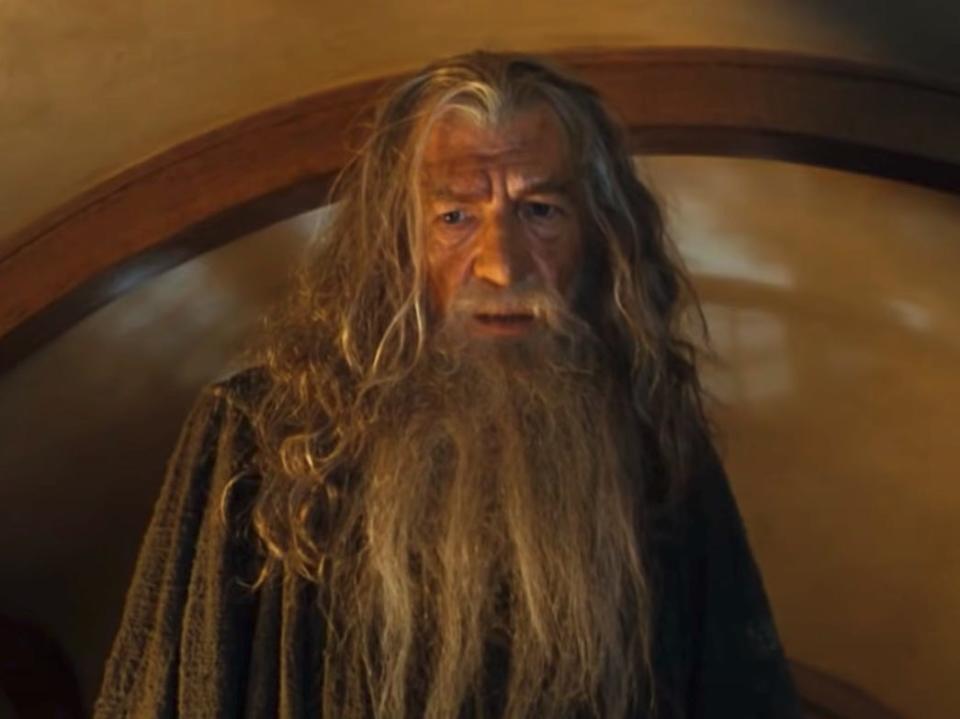 gandalf wearing a gray cloak and standing in a hobbit house in lord of the rings