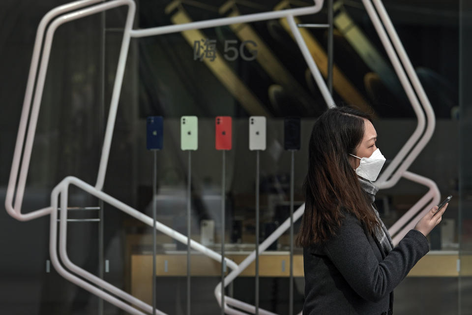 A woman wearing a face mask to help curb the spread of the coronavirus holds her smartphone as she passes an Apple store promoting its iPhone 12 devices powered with 5G at the capital city's popular shopping mall in Beijing on Wednesday, Feb. 24, 2021. (AP Photo/Andy Wong)