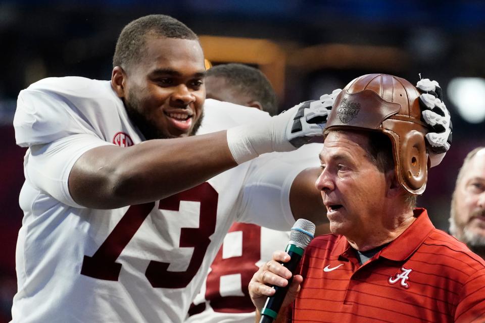 Alabama offensive lineman Evan Neal (73) places the leather helmet from the "Old Leather Helmet Torphy" on head coach Nick Saban's head after they defeated Miami in the Chick-fil-A Kickoff NCAA college football game Saturday, Sept. 4, 2021, in Atlanta. (AP Photo/John Bazemore)