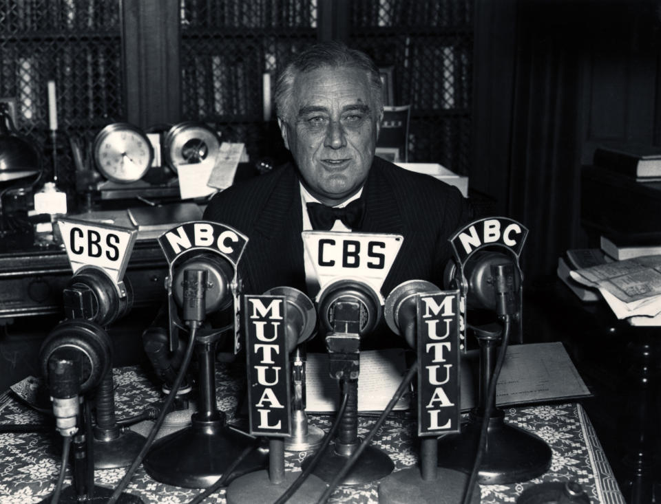 President Franklin D. Roosevelt speaking from behind a large number of radio microphones with letters such as CBS and NBC on them.