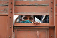 A man looks on as migrant laborers returning from other states, many of whom have been walking and hitchhiking travel on the back of a truck as they try to reach their native villages in Prayagraj, India, Sunday, May 10, 2020. Though the government started running trains to carry stranded workers to their home states, lack of trains has led many to walk back. (AP Photo/Rajesh Kumar Singh)