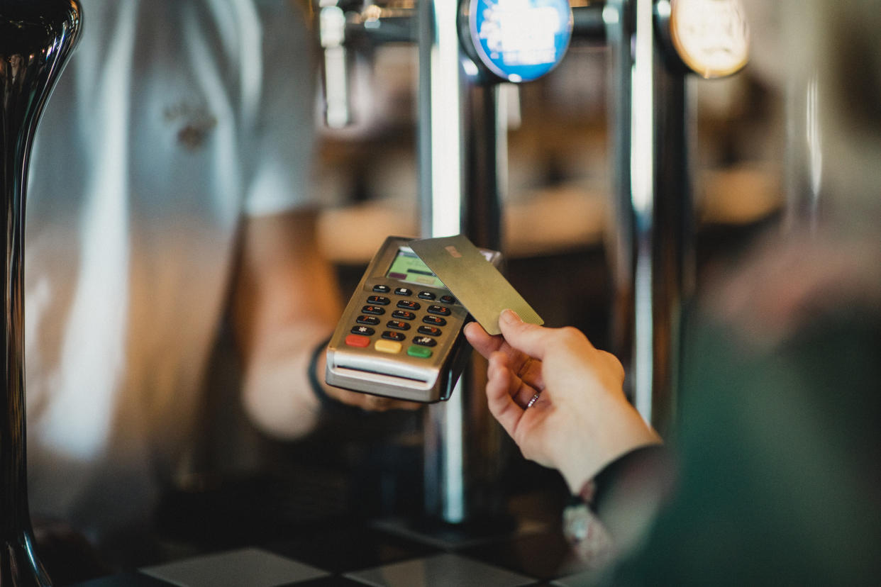 A close-up shot of an unrecognizable woman paying for a glass of red wine using contactless card payment at a bar.