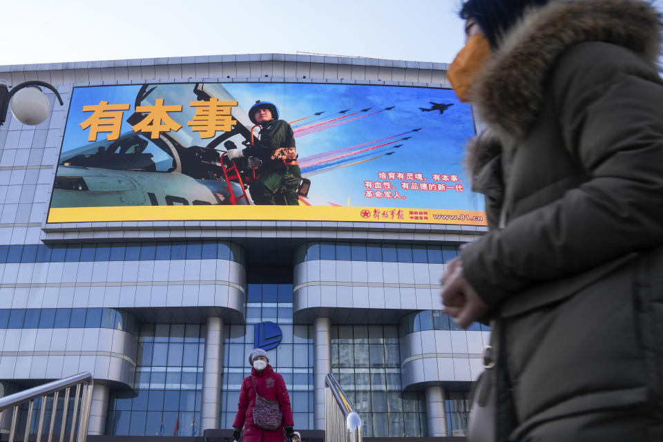 Residents wearing face masks walk by a large screen showing the Chinese People's Liberation Army Airforce outside a mall in Beijing, Monday, Jan. 9, 2023. The Chinese military held large-scale joint combat strike drills starting Sunday, sending war planes and navy vessels toward Taiwan, both the Chinese and Taiwanese defense ministries said. (AP Photo/Andy Wong)