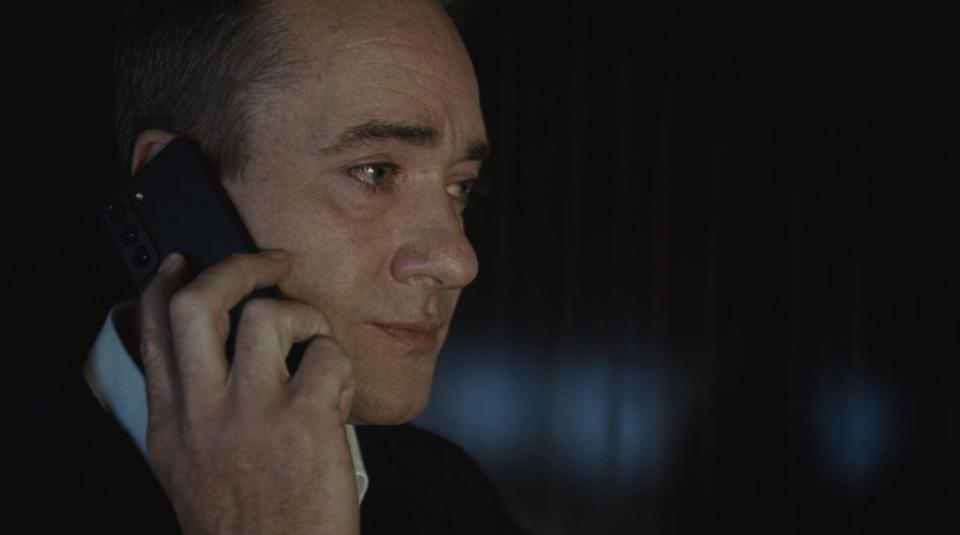 A middle-aged man talking on the phone in a dark room.