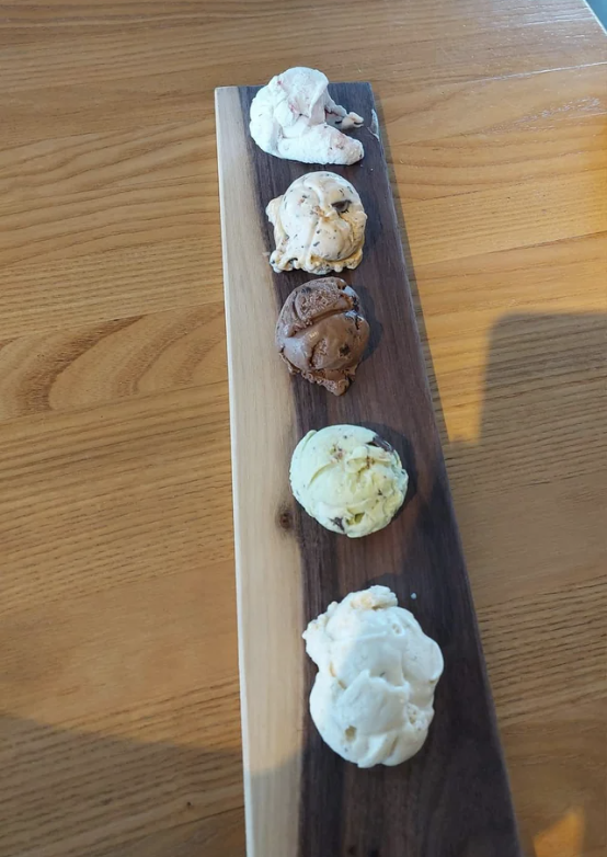 A wooden platter holds five scoops of various flavors of gelato or ice cream neatly arranged in a line