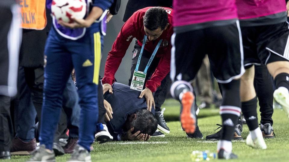 Besiktas manager Senol Gunes fell to the ground after being struck in the head by an object thrown from the stands. (AAP)