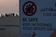 A crowd of more than 10 people gather on a beach despite a sign warning passers-by to maintain a distance from each other over the outbreak of the new coronavirus in Dubai, United Arab Emirates, Friday, March 20, 2020. The United Arab Emirates has closed its borders to foreigners, including those with residency visas, over the coronavirus outbreak, but has yet to shut down public beaches and other locations over the virus. (AP Photo/Jon Gambrell)