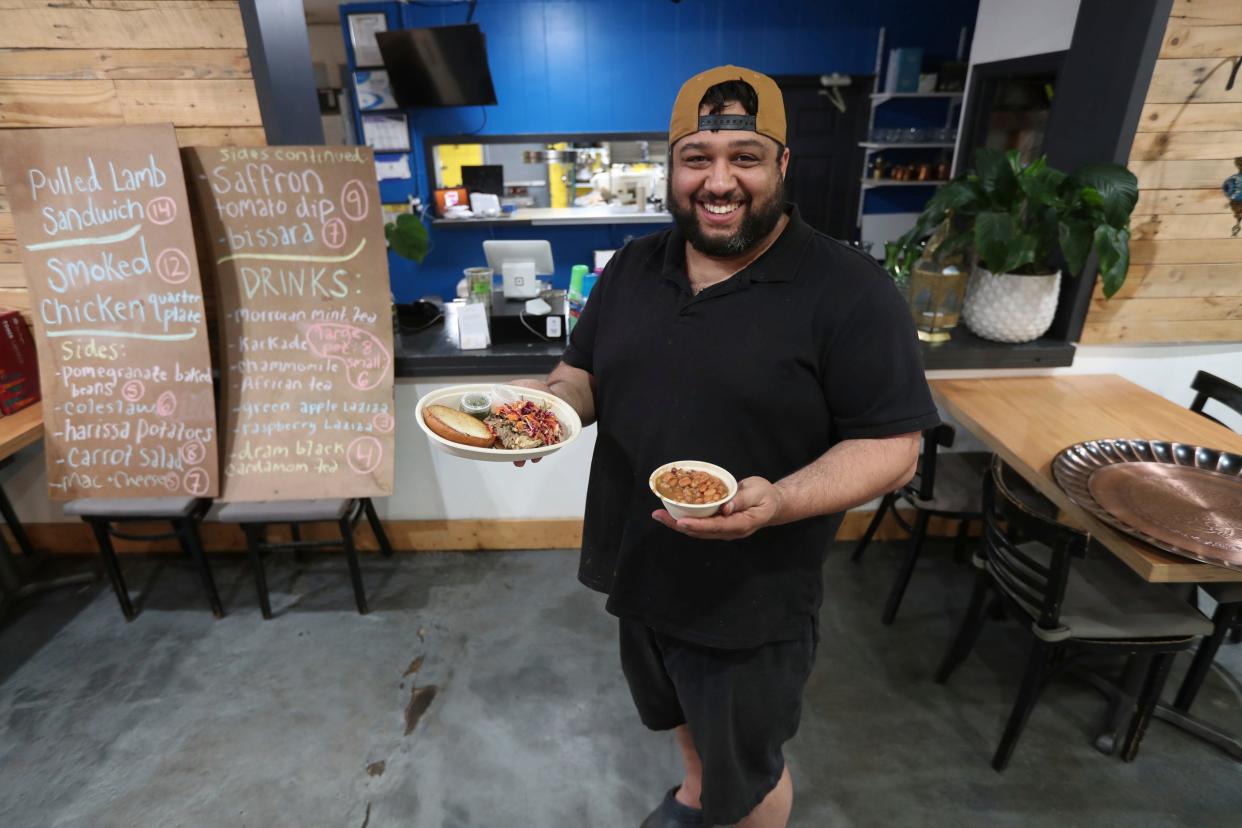 Owner and head chef Omar Anani in the kitchen of Saffron De Twah on Saturday, April 30, 2022, in Detroit. The restaurant specializes in modern Moroccan food. Anani is holding a pulled barbecue lamb sandwich and a side of beans.