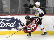 Boston Bruins center Charlie Coyle (13) checks New Jersey Devils center Janne Kuokkanen (59) to the ice during the first period of an NHL hockey game Saturday, Jan. 16, 2021, in Newark, N.J. (AP Photo/Bill Kostroun)