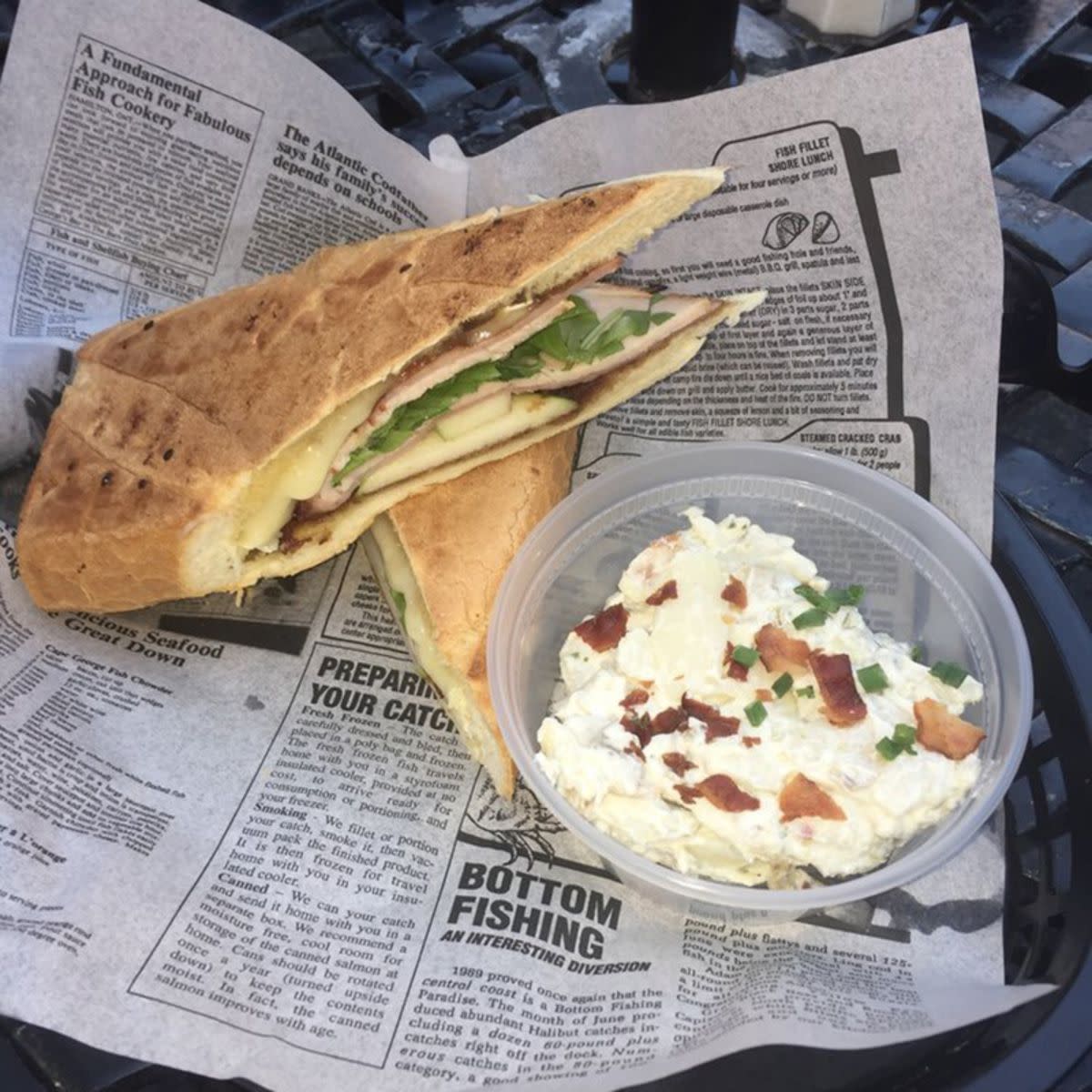 Apple 'Butter' Jeans Sandwich with a side of egg salad on a newspaper like white serving paper, Brown Dog Deli, Charleston, South Carolina, on a black plastic basket outside on a black wire table