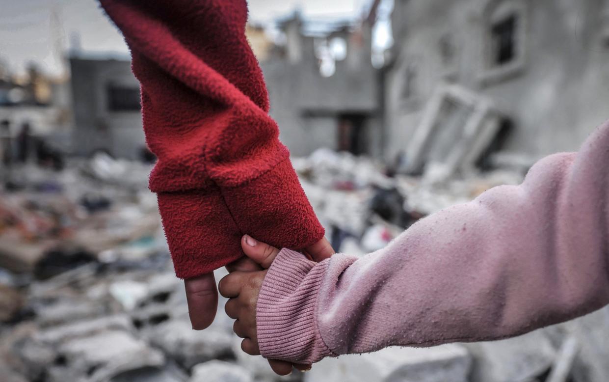 A child and an adult hold hands as they survey the destruction in Rafah, Gaza