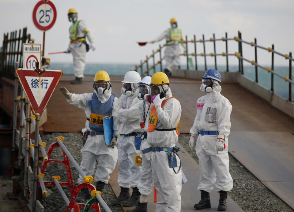 Workers, wearing protective suits and masks, stand near the No. 3 and No. 4 reactor buildings at Tokyo Electric Power Co's (TEPCO) tsunami-crippled Fukushima Dai-ichi nuclear power plant in Okuma, Fukushima Prefecture, northeastern Japan, Wednesday, Feb. 10, 2016. In one month, Japan is marking the fifth anniversary of a devastating earthquake and tsunami that hit on March 11, 2011 and left nearly 19,000 people dead or missing, turned coastal communities into wasteland and triggered a nuclear crisis. (Toru Hanai/Pool Photo via AP)