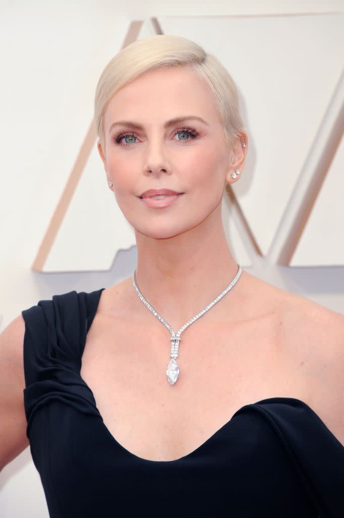 charlize theron wears a one shoulder black dress and diamond necklace on the red carpet