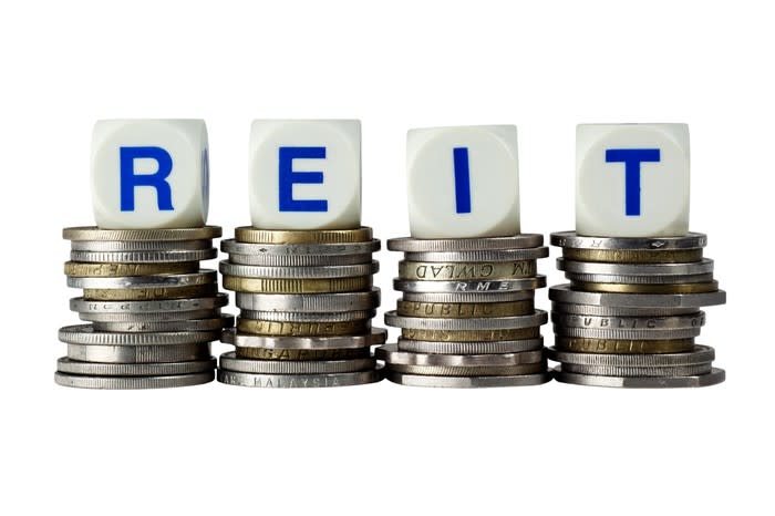 The acronym REIT spelled out with dice atop piles of coins.