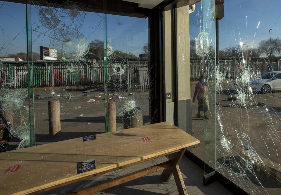 A woman wearing a face mask, walks past a damaged KFC fast food restaurant at Naledi shopping complex in Vosloorus, east of Johannesburg, South Africa, Monday, July 12, 2021. Police say six people are dead and more than 200 have been arrested amid escalating violence during rioting that broke out following the imprisonment of South Africa's former President Jacob Zuma. (AP Photo/Themba Hadebe)