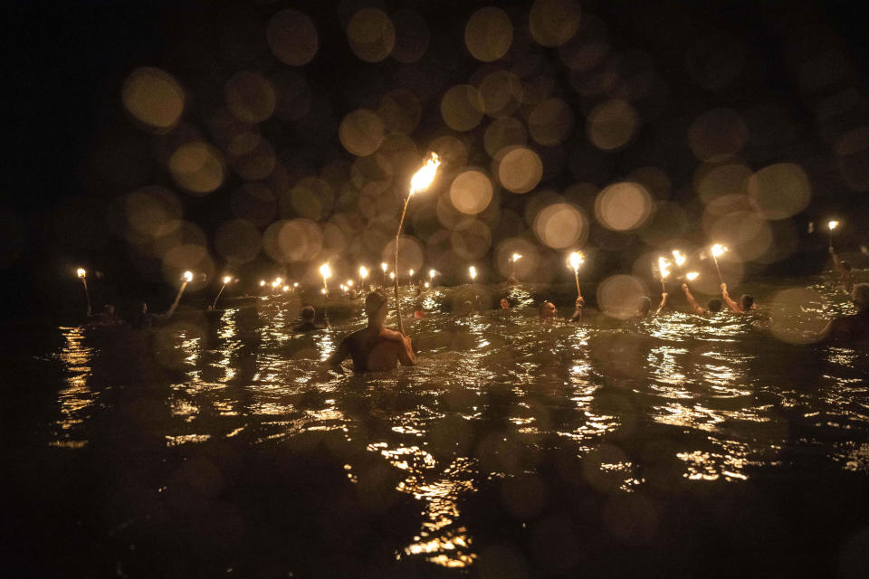 Lifeguards wade into the ocean with torches to commemorate Lifeguard Day, to honor their commitment to safety and aquatic rescue, in Mar Azul, Argentina, Wednesday, Feb. 14, 2024. (AP Photo/Rodrigo Abd)
