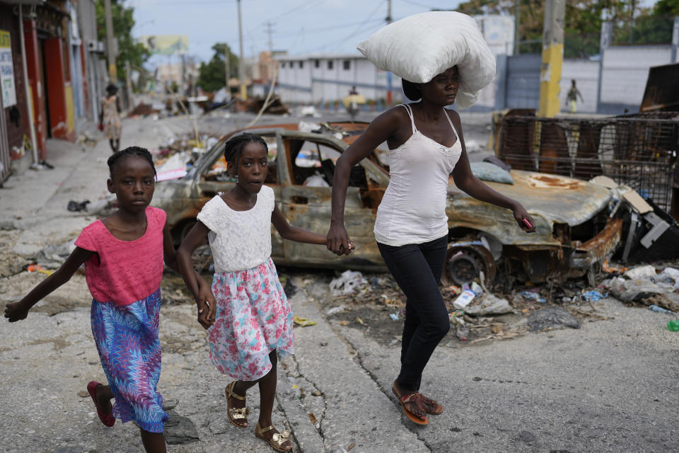 Residents walk past a burnt car blocking the street as they evacuate the Delmas 22 neighborhood the morning after an attack amid gang violence in Port-au-Prince, Haiti, May 2, 2024. (AP Photo/Ramon Espinosa)