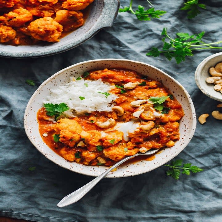 A bowl of rice topped with cauliflower tikka masala, nuts, and herbs