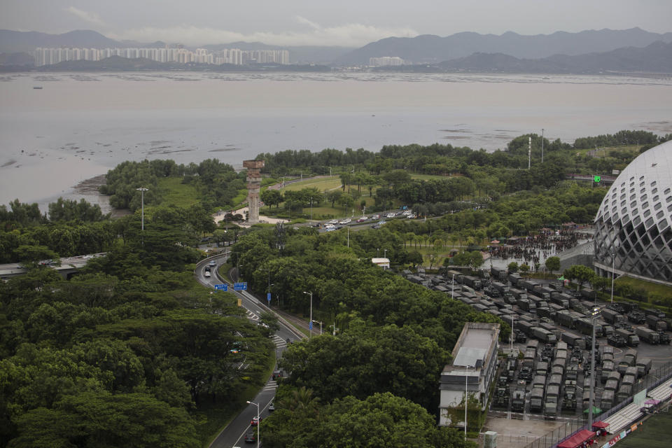 Armored vehicles and troop trucks are parked in a lot by Shenzhen Bay Stadium across from Hong Kong seen in the background in Shenzhen, Saturday, Aug. 17, 2019. One year ago, a sea of humanity - a million people by some estimates - marched through central Hong Kong on a steamy afternoon. It was the start of what would grow into the longest-lasting and most violent anti-government movement the city has seen since its return to China in 1997. (AP Photo/Ng Han Guan, File)