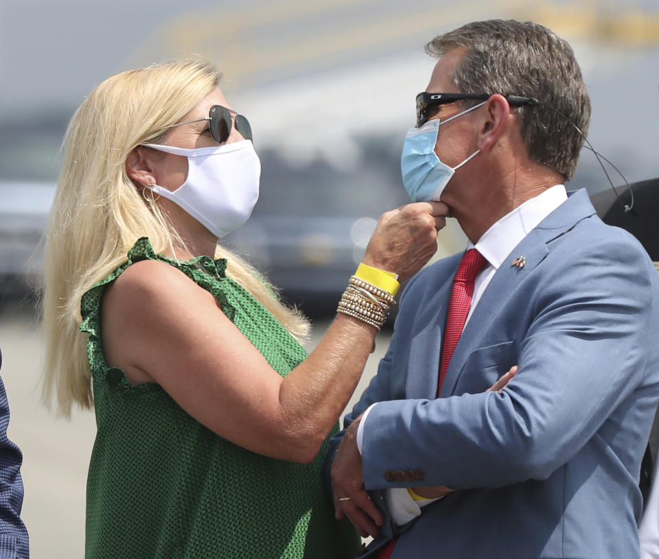 Georgia Gov. Brian Kemp has his mask adjusted by first lady Marty while waiting for President Donald Trump to arrive for his Georgia visit to talk about an infrastructure overhaul at the UPS Hapeville hub at Hartsfield-Jackson International Airport on Wednesday July 15, 2020 in Atlanta. (Curtis Compton/Atlanta Journal-Constitution via AP)