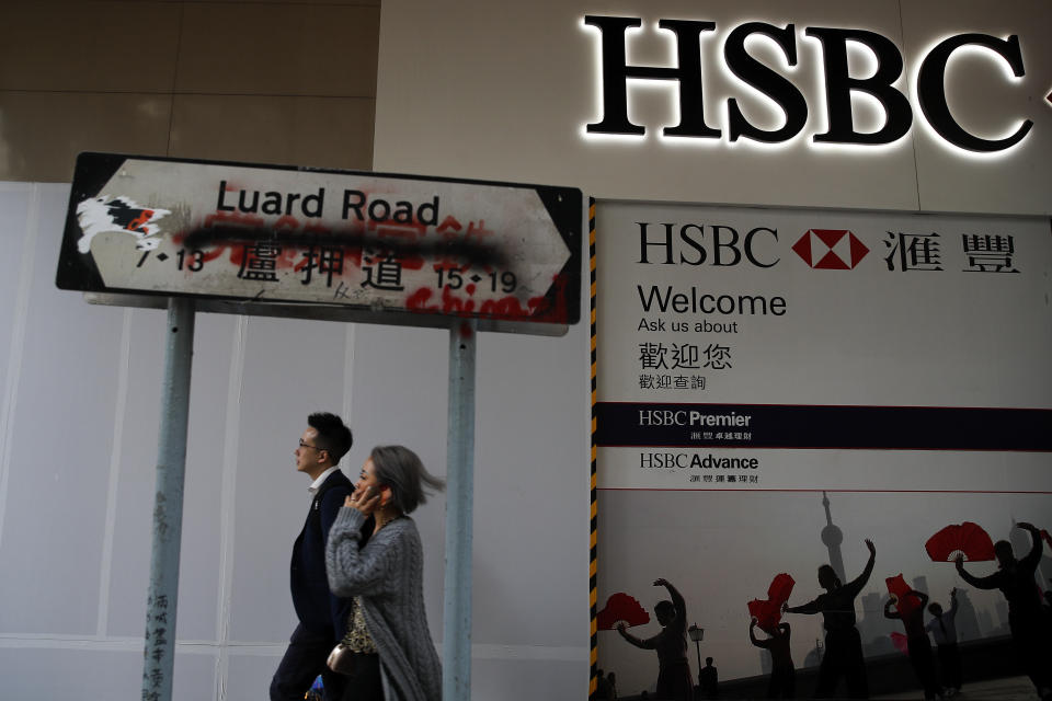 People walk by a vandalized road sign near a HSBC Bank branch covered by panels after damaged by pro-democracy protesters in Hong Kong, Saturday, Jan. 4, 2020. The months-long pro-democracy movement has extended into 2020 with further mass demonstrations. (AP Photo/Andy Wong)