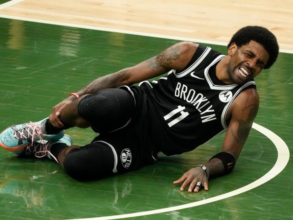 Kyrie Irving holds his ankle while lying on the floor in pain during a game.