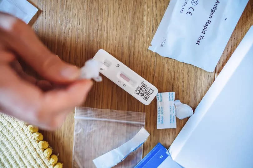 A woman squeezing the sample liquid on a test strip while carrying out a Covid-19 rapid self test at home.