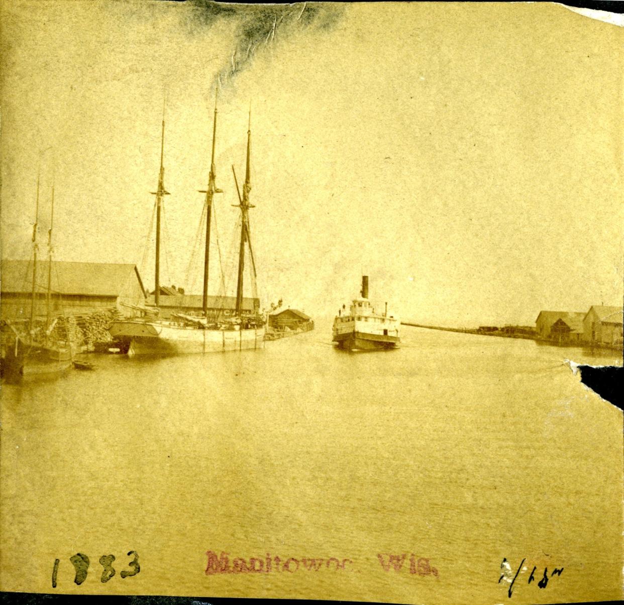 View from the Eighth Street bridge in 1883 looking east at the Manitowoc harbor. The photo shows schooners at dock on the north side of the river and a steamer entering the harbor.