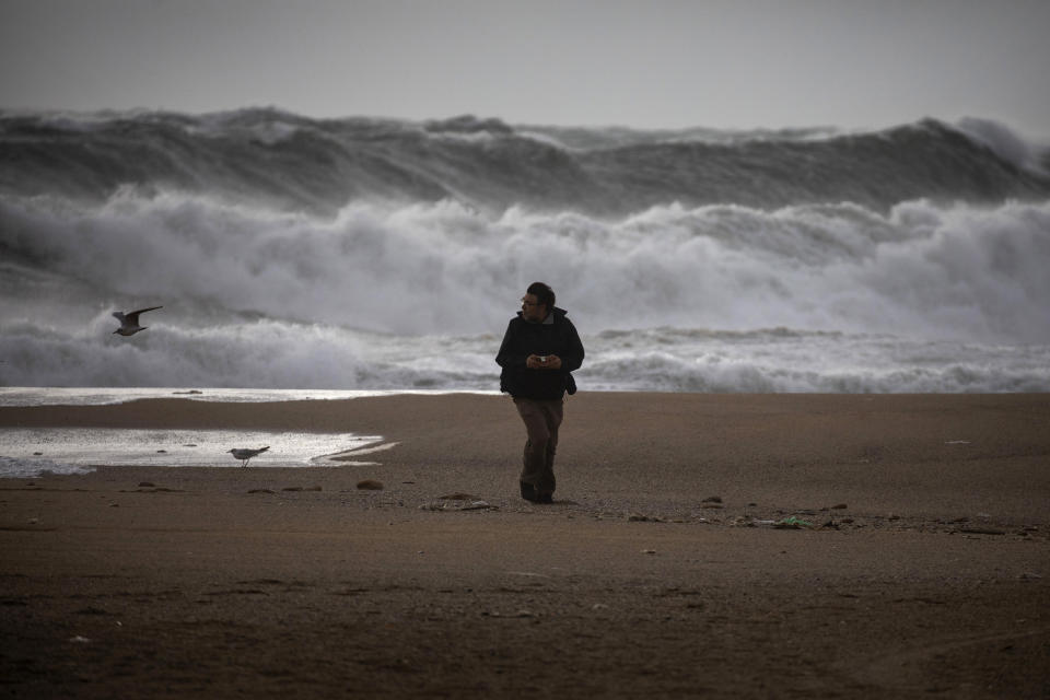 A man walks at the beach during strong winds in Barcelona, Spain, Monday, Jan. 20, 2020. Two people have died as storms carrying heavy snowfalls and gale-force winds lashed many parts of Spain on Monday. The storm has forced the closure of Alicante airport and some 30 roads in eastern region. Six provinces are on top alert. (AP Photo/Emilio Morenatti)