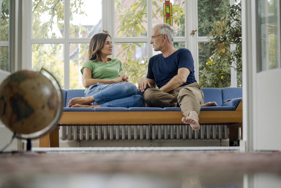 Married couple sitting and talking on sofa at home. (Getty Images)