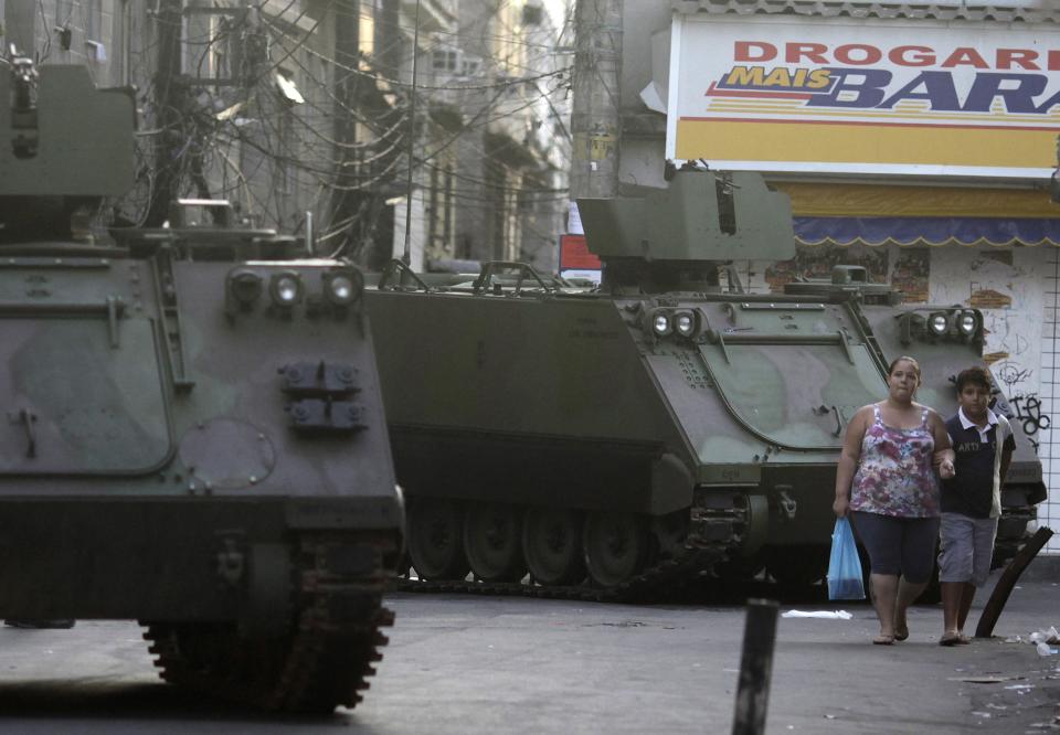 Residents walk past Brazilian Navy armored vehicles during an operation at the Mare slums complex in Rio de Janeiro March 30, 2014. The federal troops and police occupied the Mare slums complex on Sunday to help quell a surge in violent crime following attacks by drug traffickers on police posts in three slums on the north side of the city, government officials said. Less than three months before Rio welcomes tens of thousands of foreign soccer fans for the World Cup, the attacks cast new doubts on government efforts to expel gangs from slums using a strong police presence. The city will host the Olympics in 2016. REUTERS/Ricardo Moraes (BRAZIL - Tags: CRIME LAW SOCIETY)