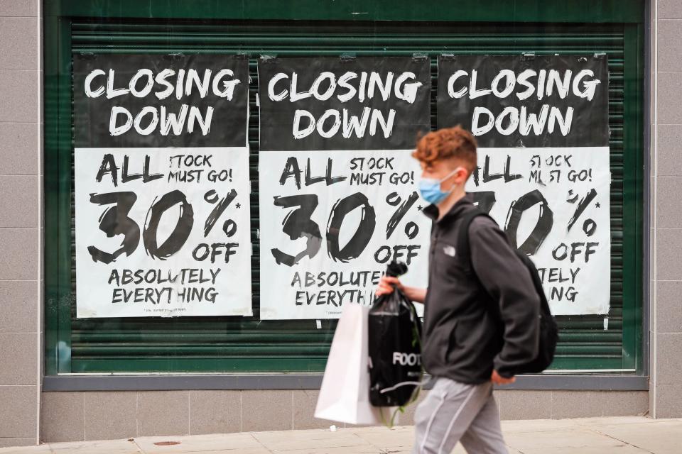 A man wearing a protective face mask walks past a shop window advertising a closing down sale in Nottingham city centre: PA