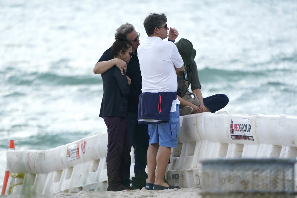 A group of people, who asked not to be identified, stand behind a barricade on the beach near the Champlain Towers South Condo building, Saturday, June 26, 2021, in the Surfside area of Miami. The apartment building partially collapsed on Thursday. (AP Photo/Lynne Sladky)