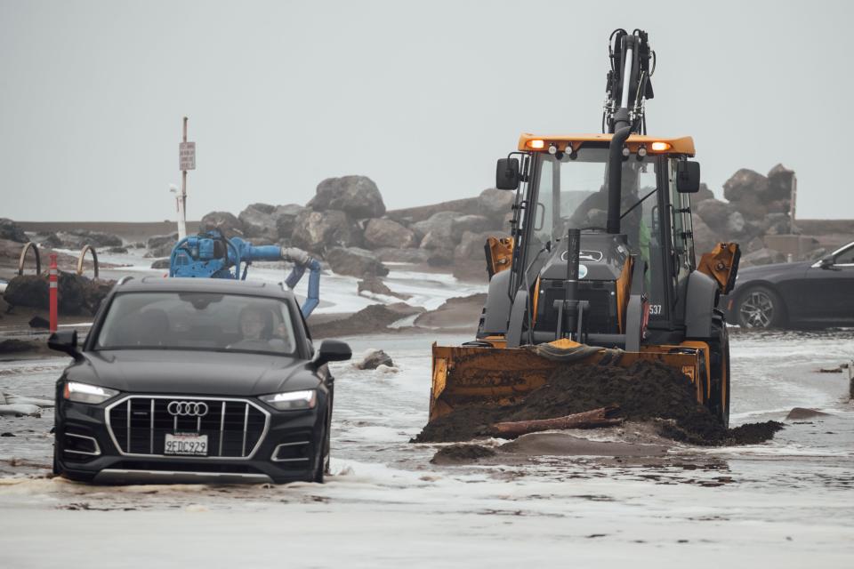 A front end loader removes debris along a flooded Clarendon road due to high waves in Pacifica, Calif., Thursday, Dec. 28, 2023. Powerful surf is rolled onto beaches on the West Coast and Hawaii as a big swell generated by the stormy Pacific Ocean pushes toward shorelines.