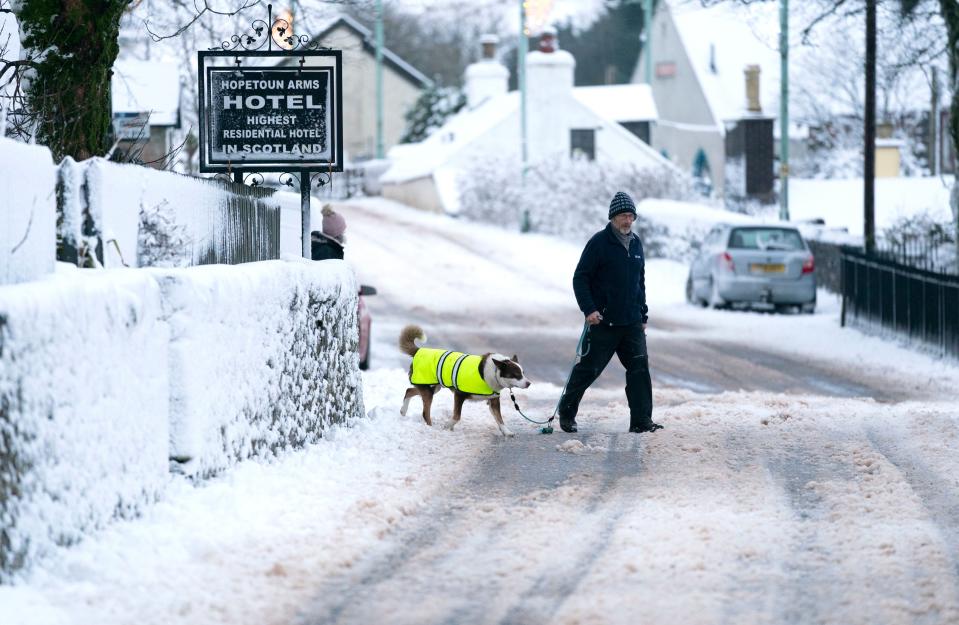 A man walks his dog through the snow in Leadhills (PA)