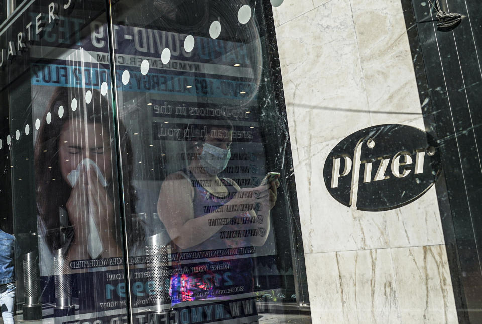 FILE - In this Nov. 9, 2020, file photo, an ad for COVID-19 testing reflects on glass at a bus stop, as pedestrians walk past Pfizer world headquarters in New York. Pfizer and BioNTech say they've won permission Wednesday, Dec. 2, 2020, for emergency use of their COVID-19 vaccine in Britain, the world’s first coronavirus shot that’s backed by rigorous science -- and a major step toward eventually ending the pandemic. (AP Photo/Bebeto Matthews, File)