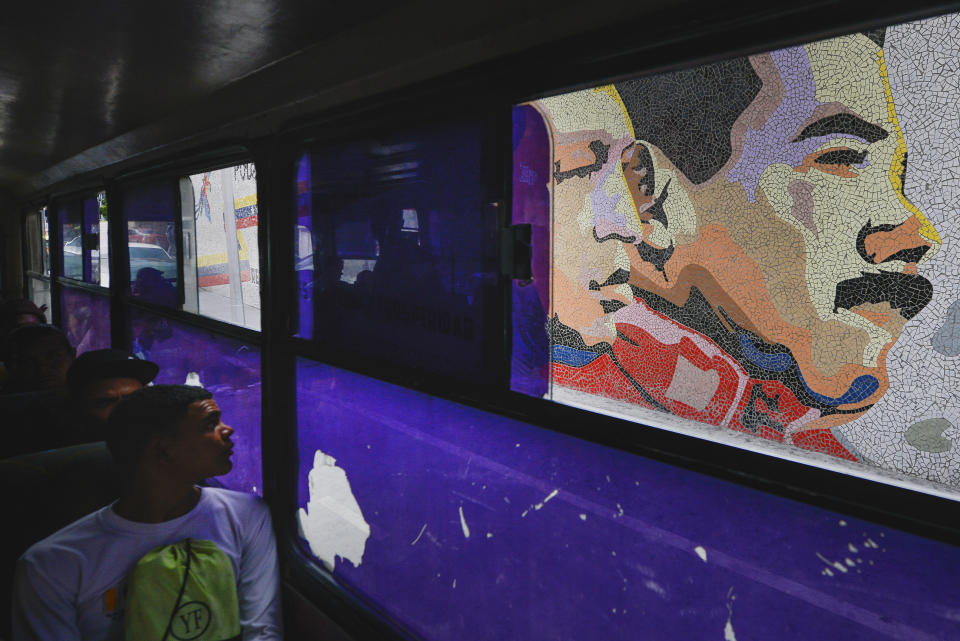 In this Dec. 19, 2019 photo, a man sitting on a bus looks at a mosaic of late leader Hugo Chavez, left, and of Venezuela's President Nicolas Maduro, right, in Caracas, Venezuela. Maduro, whose approval ratings in the polls have dipped close to 10%, has proven more resilient than many expected. (AP Photo/Matias Delacroix)