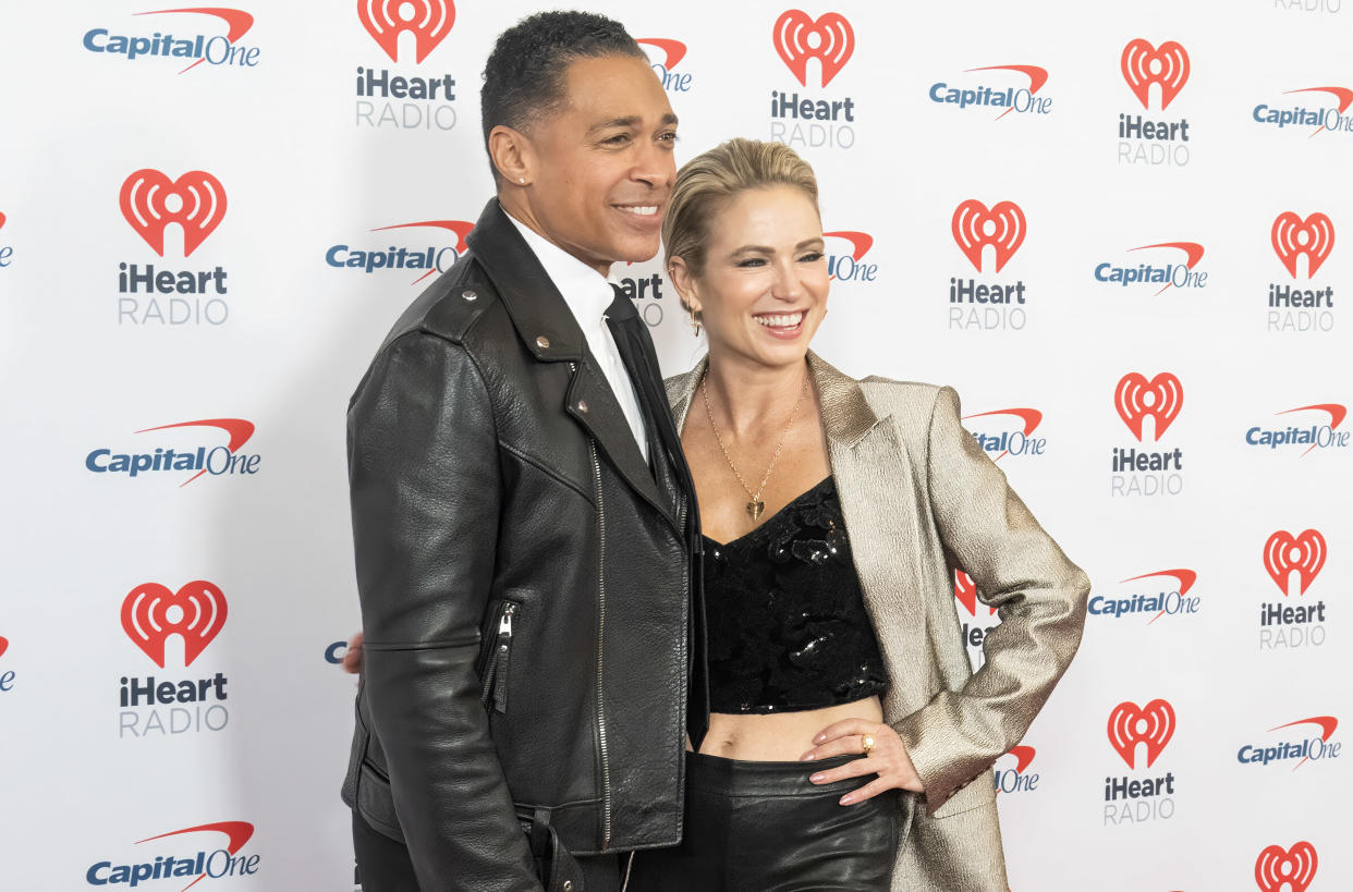 T.J. Holmes and Amy Robach standing together in front of signage that reads: iHeartRadio.